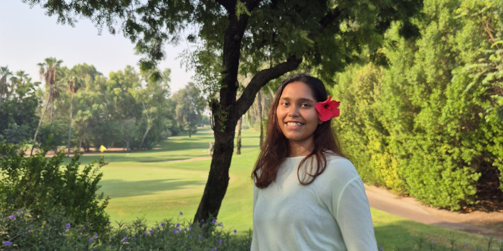 Ash Carnie smiling in a garden in the morning light, with open lawn and palms behind her